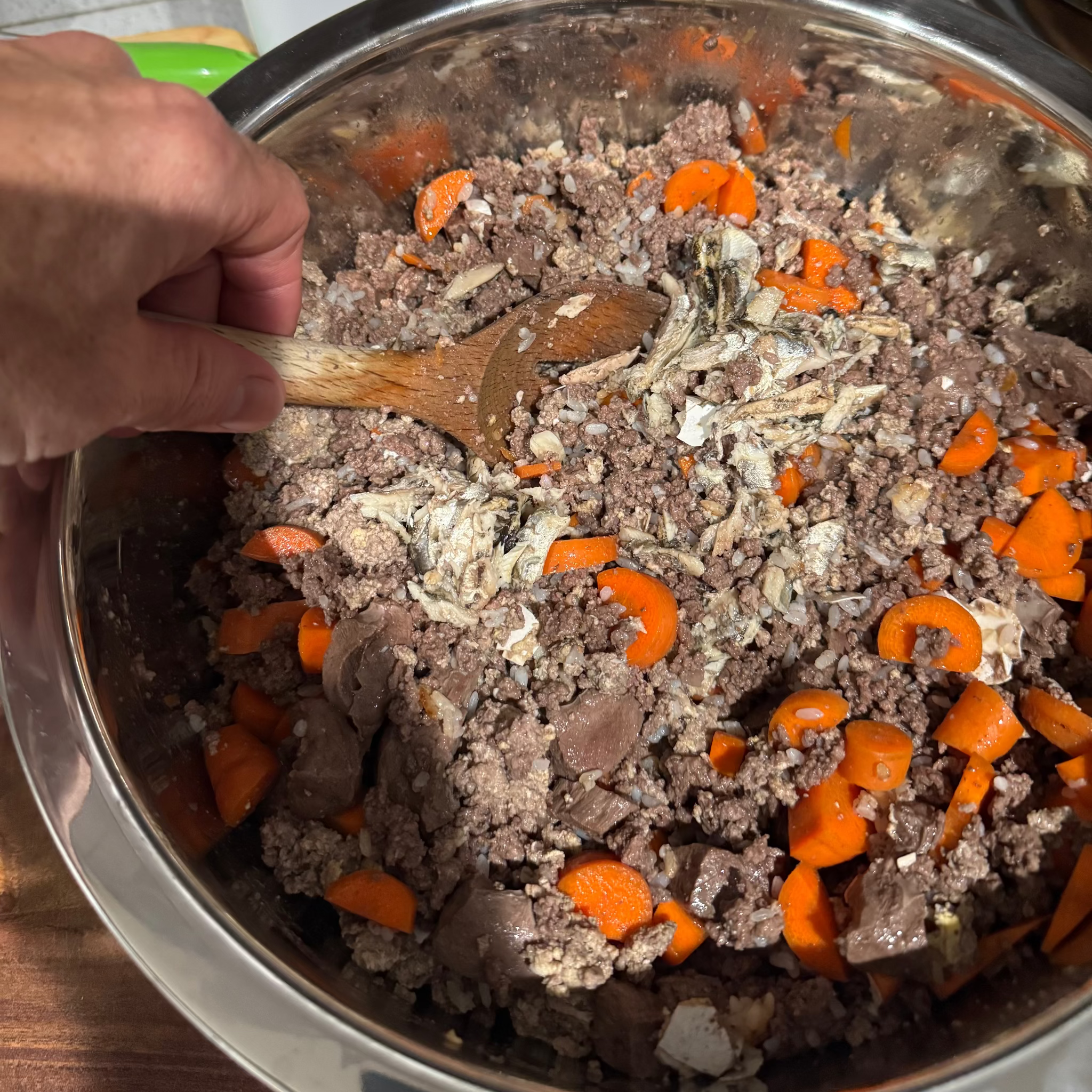 Stirring ground meat with carrots in a metal bowl.